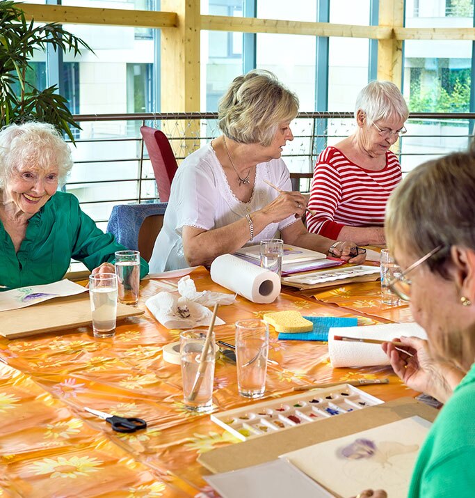 A group of women gathered around a table, happily painting together with colorful supplies.